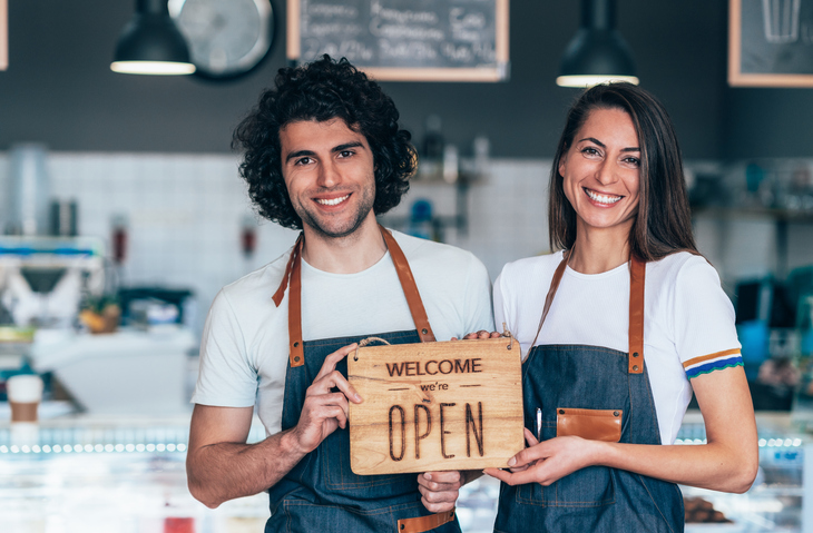 Portrait of two proud coffee shop owners, beautiful couple holding up a sign on opening day